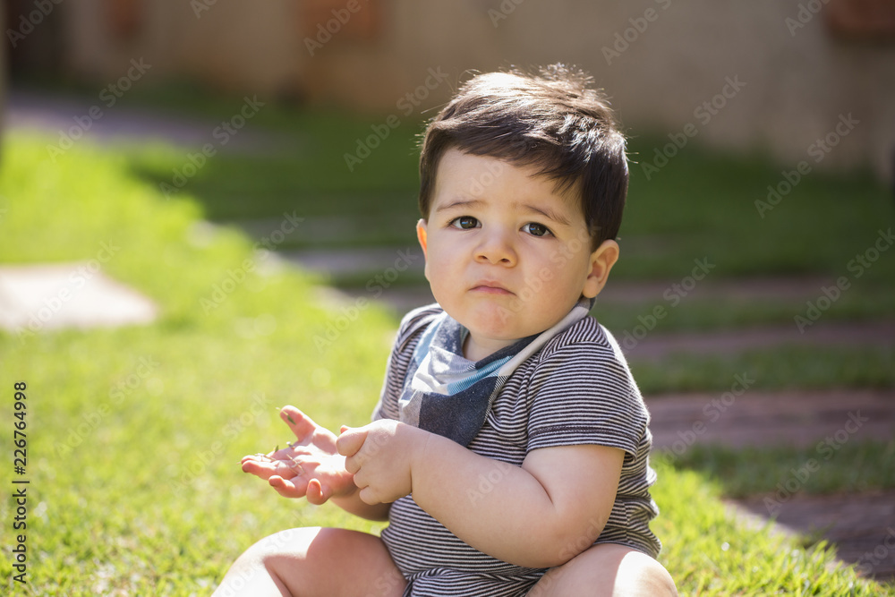 Beautiful brazilian baby boy in the grass looking at camera. Serious baby Beautiful brazilian baby boy in the grass looking at camera. Serious baby