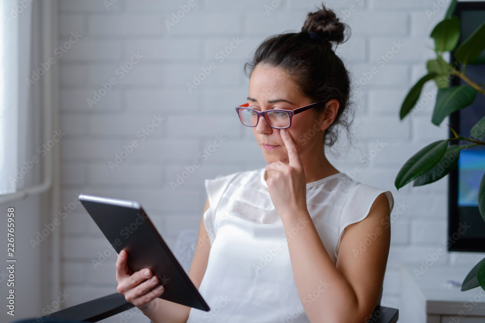 Serious middle age woman sitting in a chair and looking at tablet. Serious middle age woman sitting in a chair and looking at tablet.
