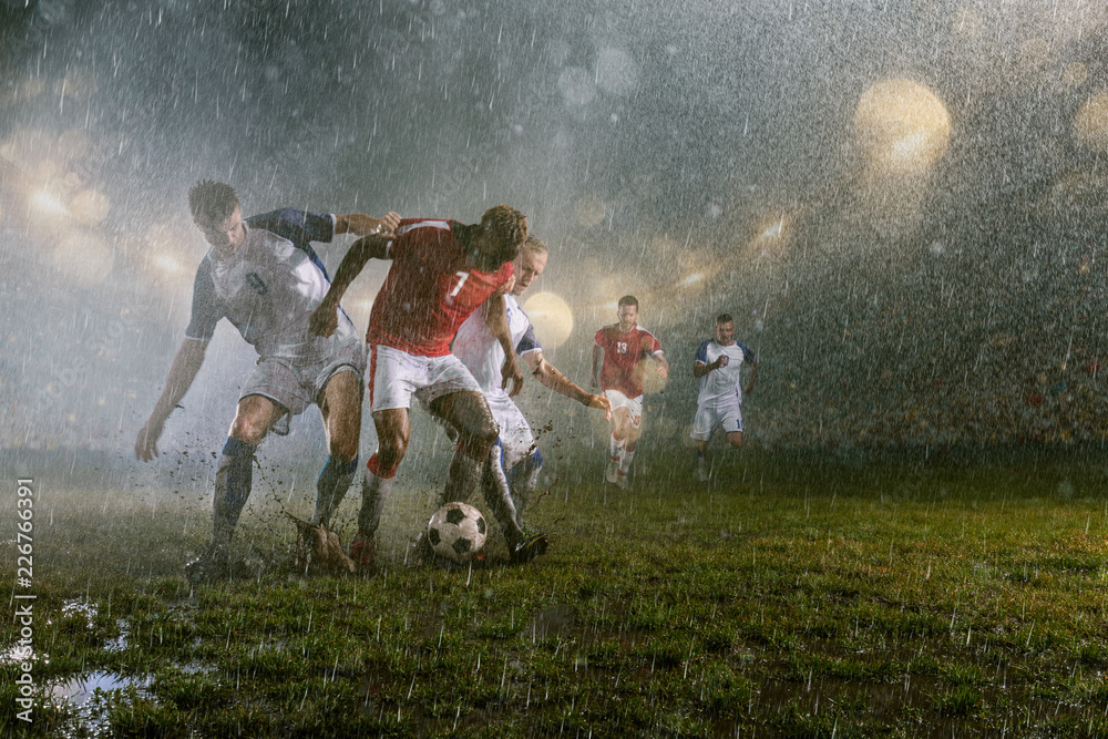 Soccer players performs an action play on a professional night rain stadium. Dirty players in rain drops scores a goal. Grass in the stadium wet from the rain