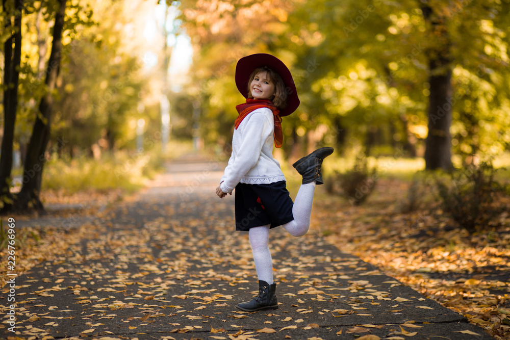 Adorable little girl in red hat walk in autumn beauty park