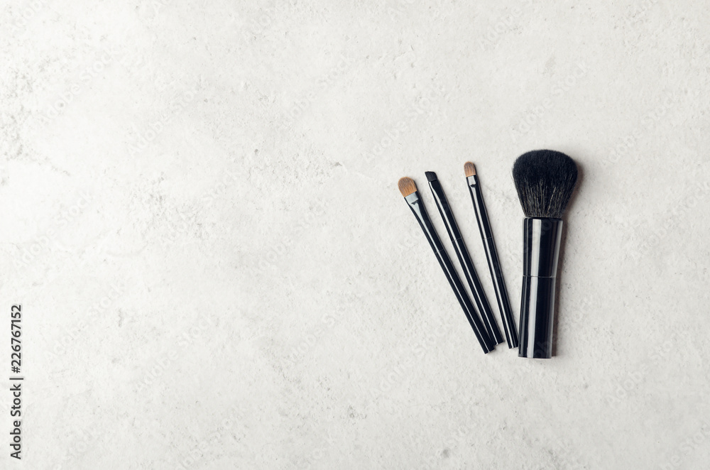 Black makeup brushes on a light stone background. Professional tools for make-up artist. Flat Lay, top view, copy space.