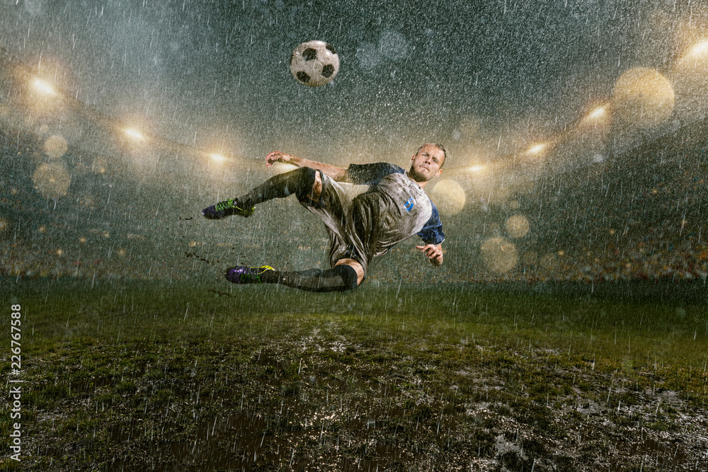 Soccer player on professional soccer night rain stadium. Dirty player in rain drops kicks the football ball in flight