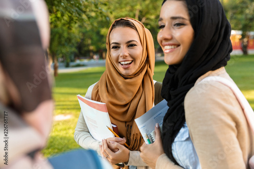 Canvas Print Cheerful young arabian women students holding books in park outdoors talking with each other