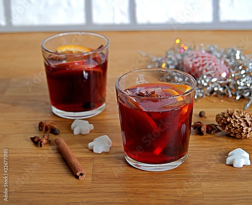 Mulled wine, heated red wine with slices of apple and orange, cinnamon sticks and anise in glass cups on wooden background.