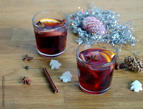 Mulled wine, heated red wine with slices of apple and orange, cinnamon sticks and anise in glass cups on wooden background.