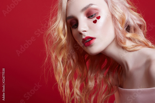 Portrait of sexy fashion beautiful blonde woman with bright makeup posing on red crimson background. Slender blonde girl, perfect figure and long hair. Clean perfect face skin