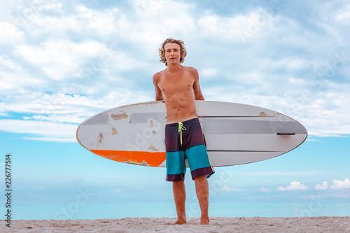 Canvas Print Handsome man walk with white blank surfing board wait for wave to surf spot at sea ocean shore