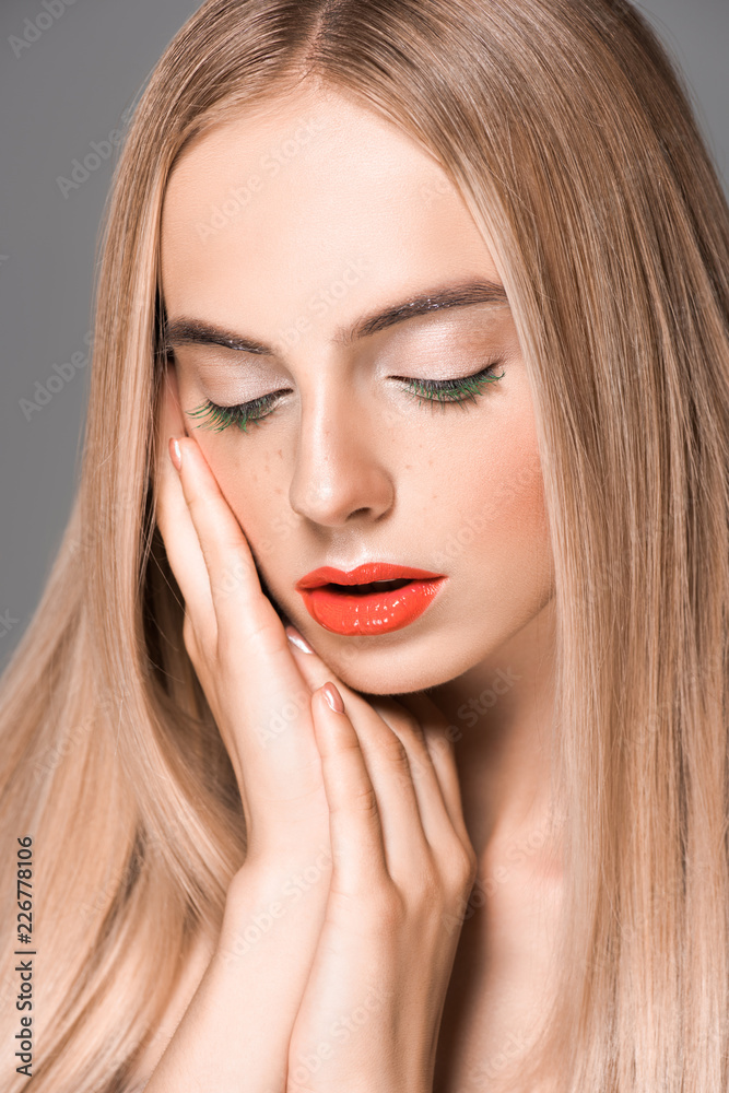 beautiful tender girl with long smooth hair looking down isolated on grey