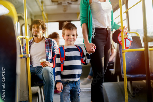Picture of cute little boy in a bus. Looking at he camera and holding his mothers hand.