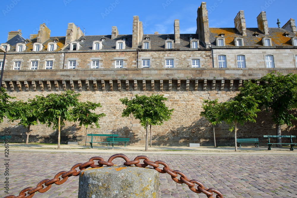 View of Traditional houses with chimneys inside the walled city of Saint Malo, with the cobbled pavement of Robert Surcouf Esplanade in the foreground, Saint Malo, Brittany, France - obrazy, fototapety, plakaty 