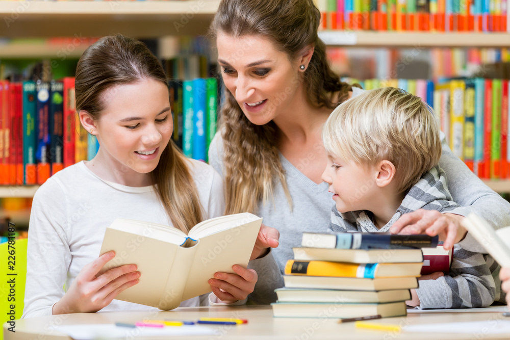 Teacher with her class visiting the library reading books for education Teacher with her class visiting the library reading books for education