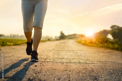 Young fitness woman trail running on the rural road in summer with sunset background
