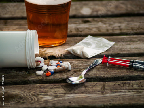 A glass of beer, pills, barbiturates, drugs, cocaine, heroin, a syringe and a spoon on a table. Drug addiction concept photo