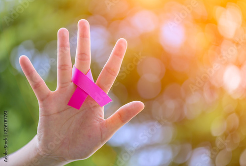 Woman hands holding pink ribbon on green bokeh background for supporting breast cancer awareness month campaign.