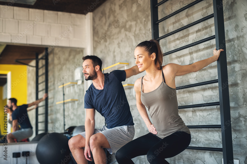 Beautiful young athlete couple holding for a bar and stretching their arm muscles after training in a gym. Beautiful young athlete couple holding for a bar and stretching their arm muscles after training in a gym.