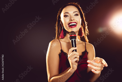 portrait of excited beautiful woman with microphone in hand singing karaoke