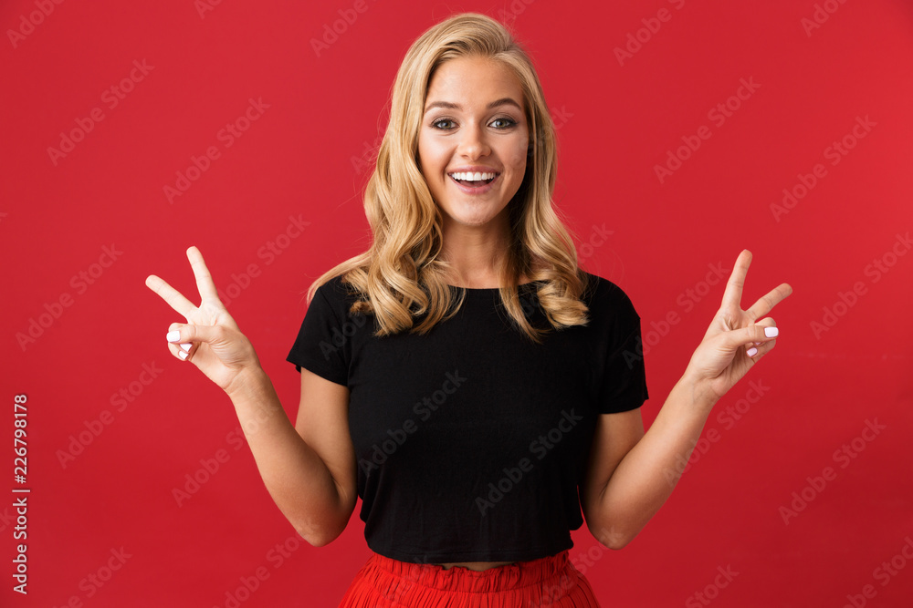 Portrait of attractive woman 20s smiling and showing peace sign, isolated over red background in studio Portrait of attractive woman 20s smiling and showing peace sign, isolated over red background in studio