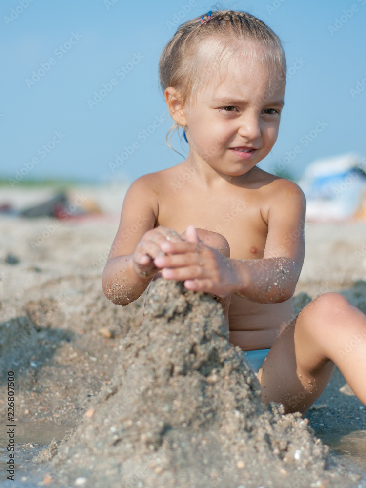 Baby girl sitting on the sandy beach and playing near the sea. Summer vacations concept. Baby girl sitting on the sandy beach and playing near the sea. Summer vacations concept.