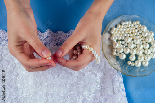 close-up hands of woman seamstress tailor ( dressmaker) designer wedding dress sews pearl beads to lace on a blue background in the studio
