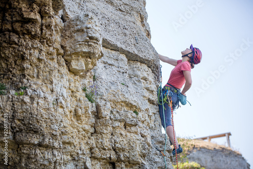 Photo of side view of young athlete woman in red helmet climbing up mountain