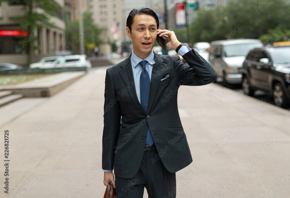 Asian businessman in city walking talking on cell phone