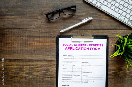 Social security benefits. Application form near pen and glasses on dark wooden background top view copy space photo