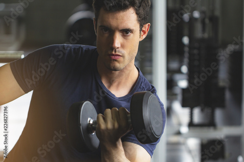 Young Man lifting dumbbells in gym, healthy lifestyle concept, With many gym equipment as background.