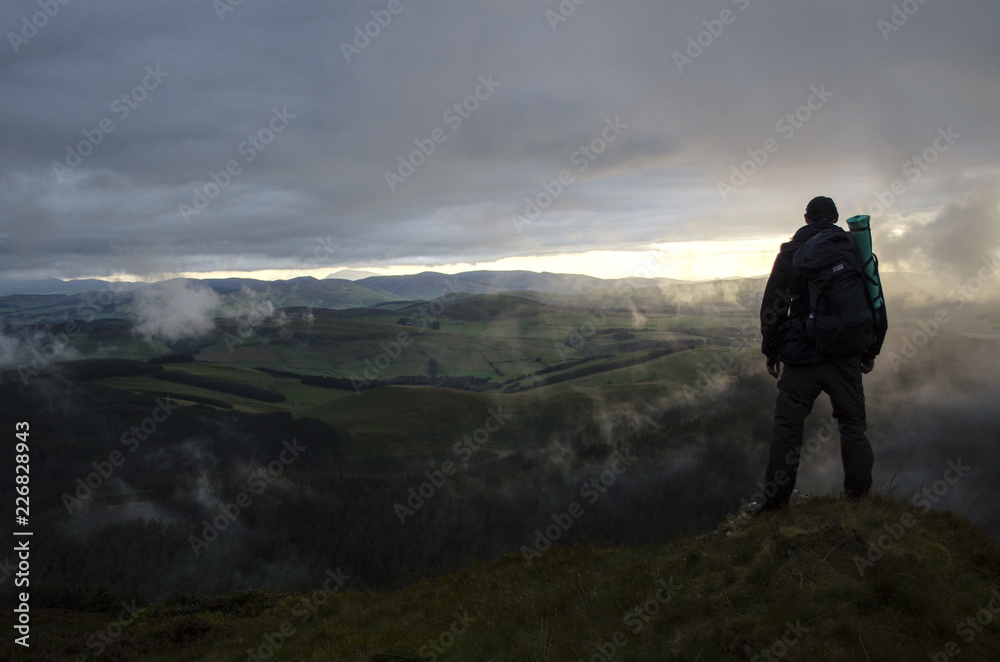 Hiker Looking Over Green Hills at Sunset