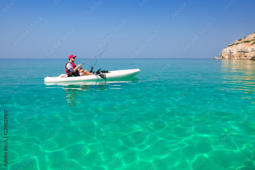 Man fishing on a kayak in the sea with clear turquoise water. Fisherman kayaking in the islands. Leisure activities on the ocean.