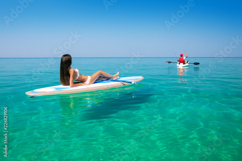 Beautiful woman on the Standup paddlbording relaxing in the sea with clean water and looking at the floating kayak. Leisure activities in the tropical ocean islands on surf.