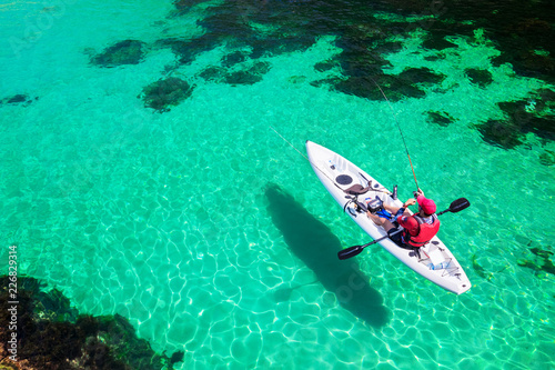 Man fishing on a kayak in the sea with clear turquoise water. Fisherman kayaking in the islands. Leisure activities on the ocean.