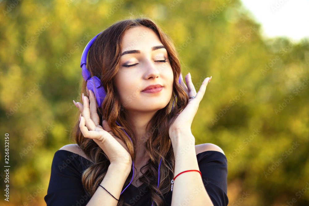 portrait of a beautiful teenager girl with headphones on head, young woman listening to music on the nature