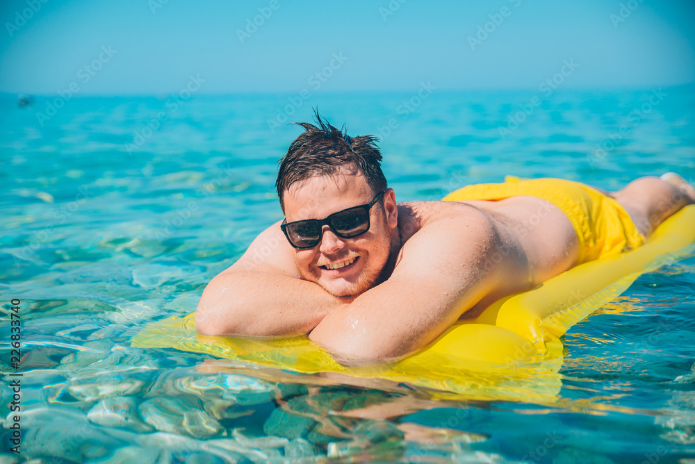 young man at yellow inflatable mattress in clear transparent water