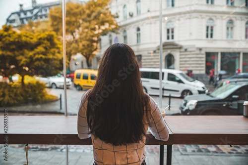 woman sitting in cafe with big glass window and beautiful view of autumn city street