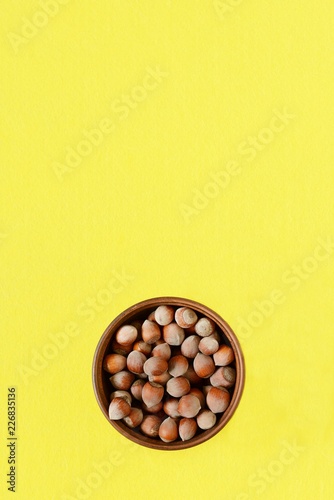 bowl with hazelnut on a yellow background. Healthy eating. Close-up, copy space, view from above. Unpeeled walnut. © VIKTORIIA DROBOT
