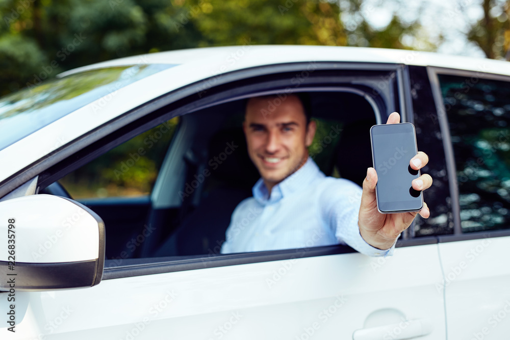 A young man sitting in a car shows a cellphone