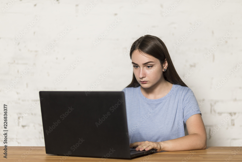 Serious girl sitting at table working on laptop Serious girl sitting at table working on laptop