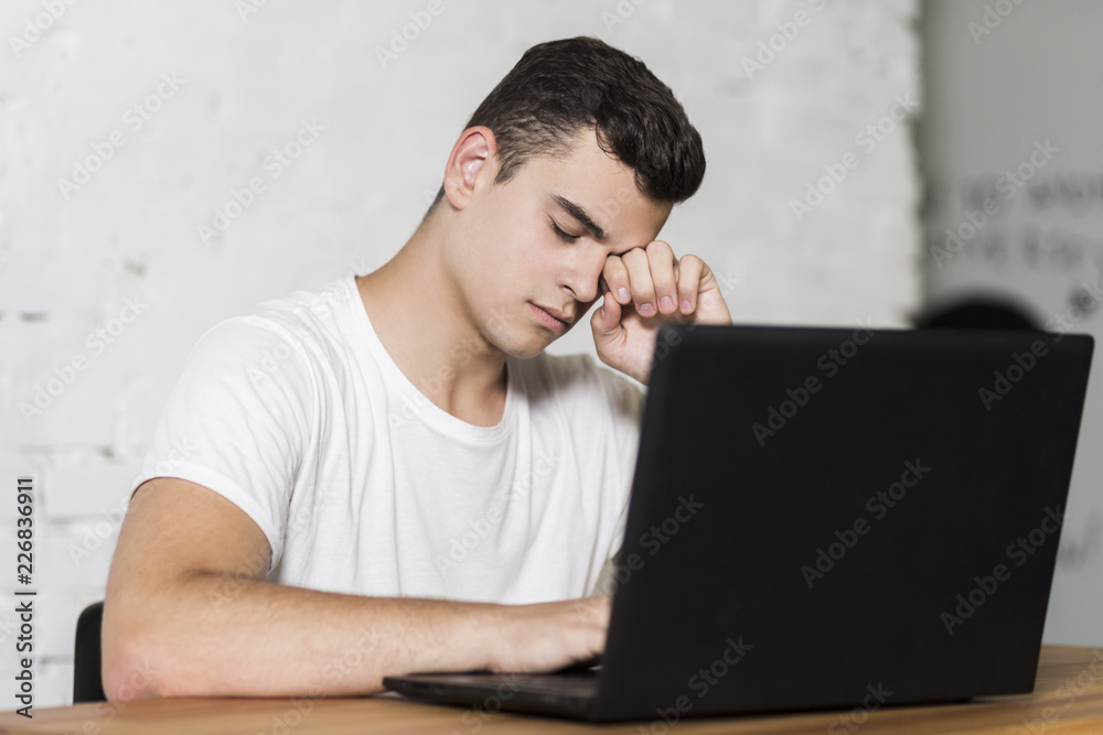 Young guy sitting at the table. He's tired of working on his laptop. Young guy sitting at the table. He's tired of working on his laptop.