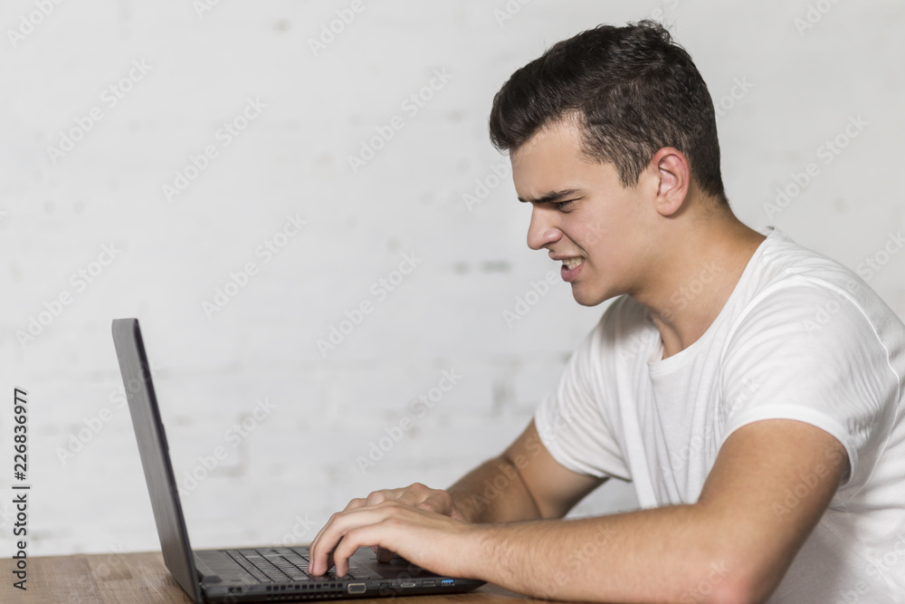 A young guy works on a laptop. He's angry. A young guy works on a laptop. He's angry.