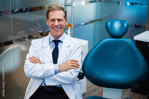 Expertise at work. Cheerful dentist looking at camera with smile while sitting in dentist’s office © MARIIA