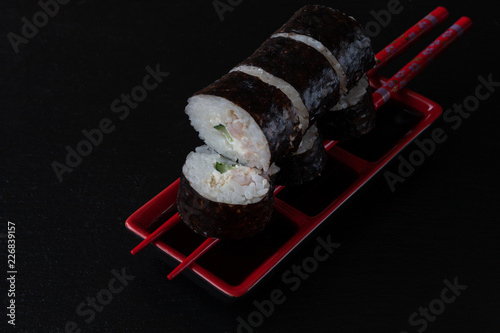 Japanese sushi with soy sauce on red bowl and chopsticks. Cose up on black concrete stone background