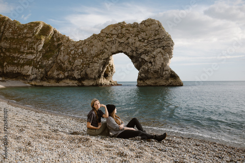 two woman sitting on a beach looking at the durdle door sea cliff arch in england