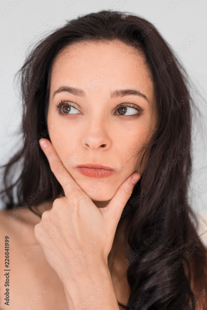 Fototapeta premium Caucasian girl with long dark hair without clothes on a white background. The girl in thoughts. Emotional shot.