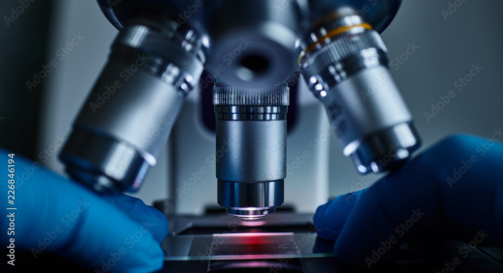 Scientist hands with sample slide on microscope close-up shot in the laboratory Scientist hands with sample slide on microscope close-up shot in the laboratory