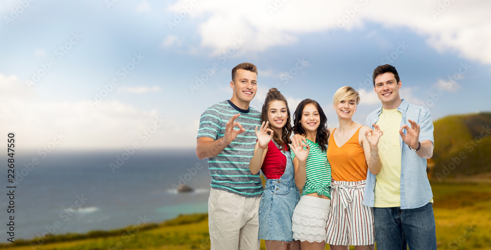 travel, tourism and summer holidays concept - group of happy smiling friends over big sur coast of california background showing ok hand sign