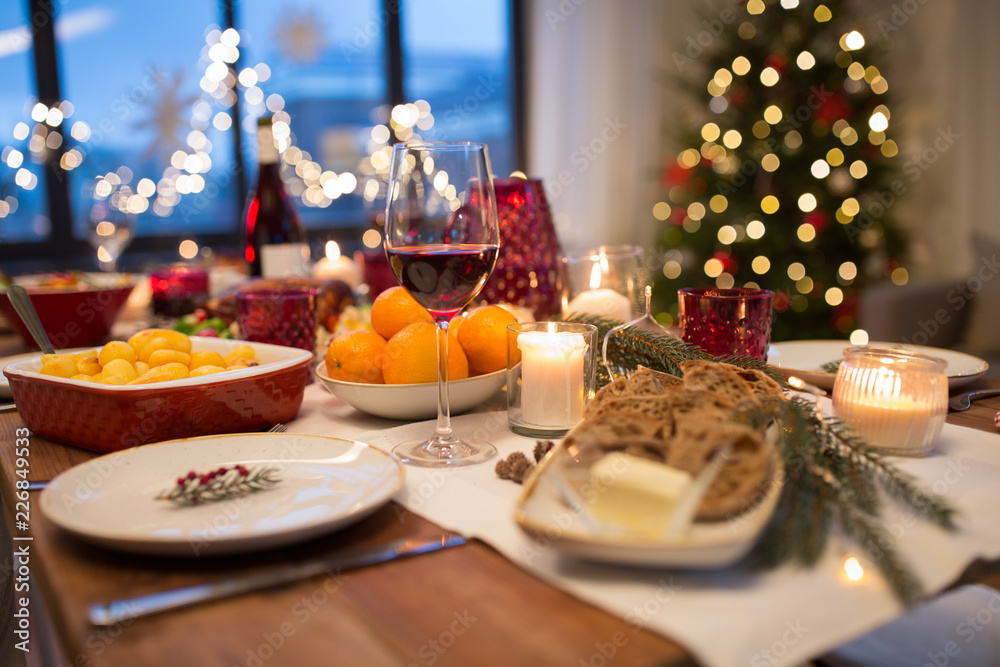 Fototapeta Świąteczny obiad i jedzenie koncepcja - kieliszek czerwonego wina i jedzenie na stole w domu