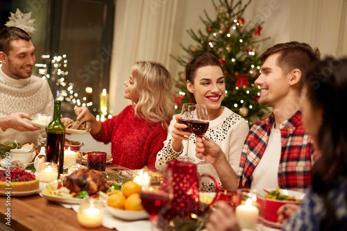 holidays and celebration concept - happy friends having christmas dinner at home, drinking red wine and clinking glasses