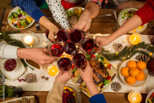 holidays and celebration concept - close up of friends having christmas dinner at home, drinking red wine and clinking glasses