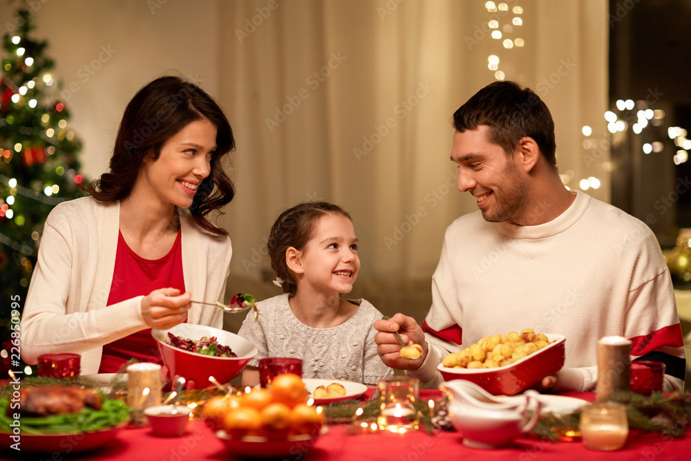 holidays, family and celebration concept - happy mother, father and little daughter having christmas dinner at home