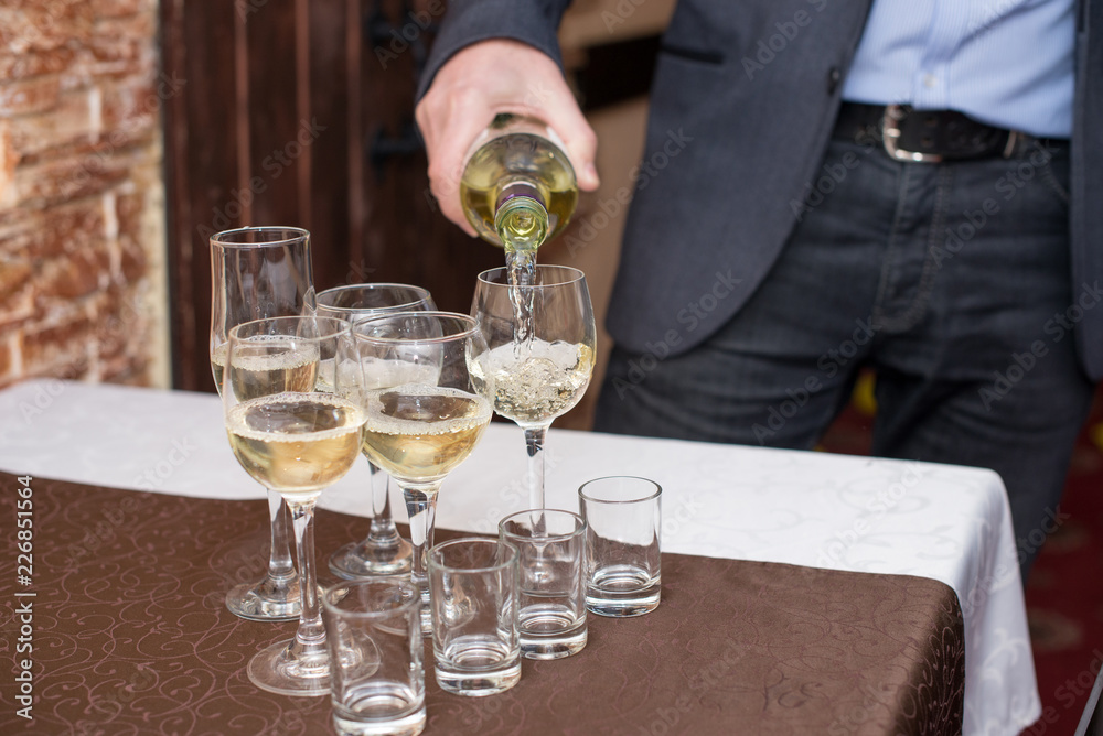 Man's hand pours champagne, white wine from bottle in wineglasses on table Man's hand pours champagne, white wine from bottle in wineglasses on table